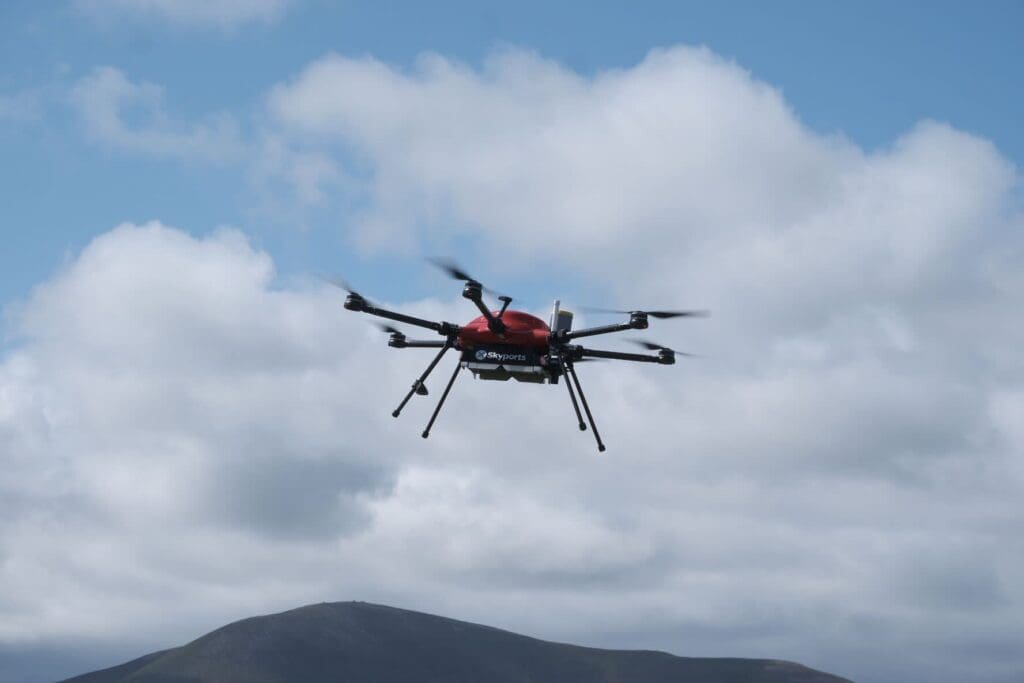 Red drone flying against cloudy sky.