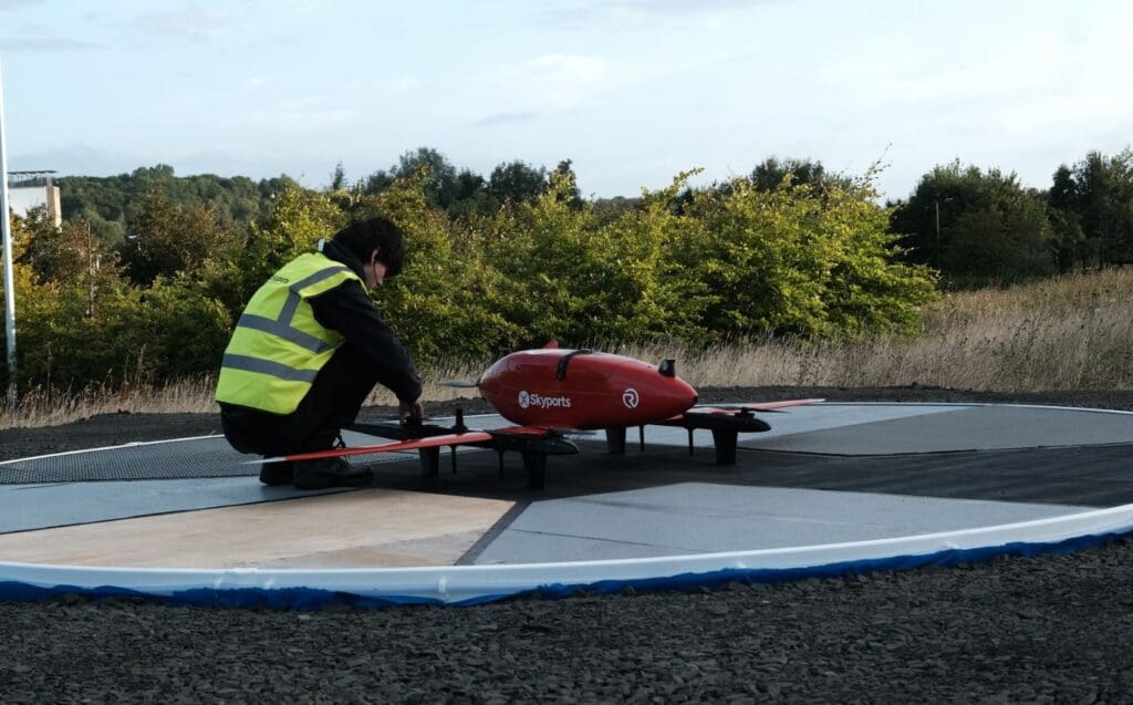 Person inspecting a red drone on landing pad.