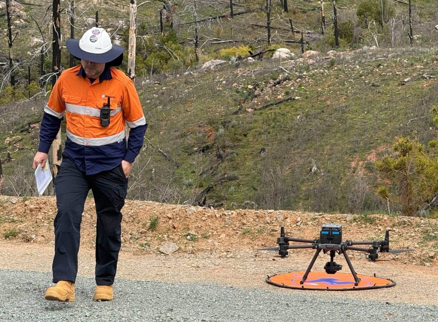 Worker walking near drone in rugged area.