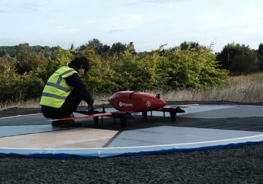 Person inspecting a red drone on landing pad.